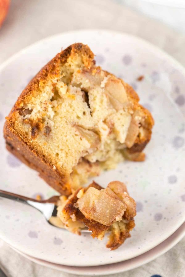 une tranche de gâteau aux pommes fait maison facile à base de jus d'orange et de pommes fraîches avec une fourchette retirée et la fourchette reposant sur l'assiette