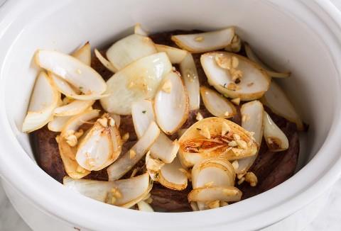 Agregue las cebollas salteadas y el ajo sobre el chuck asado en la olla de cocción lenta.