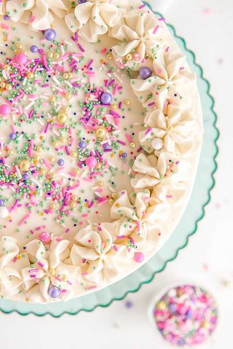 Encima de la imagen de un pastel blanco con crema de mantequilla blanca, rosetones, y espolvorea.
