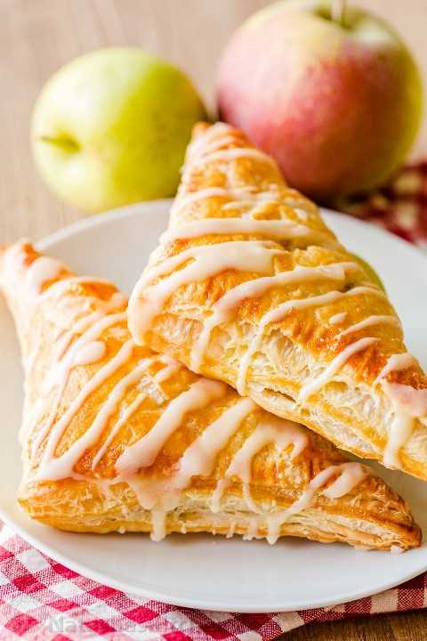 Two apple turnovers on a plate with apples in background