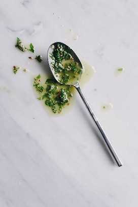 Aderezo de albahaca en una cuchara para hacer una receta de ensalada de papa sin mayonesa.