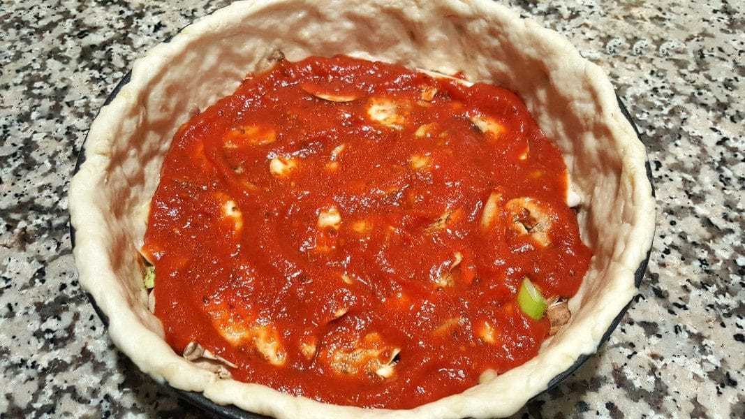 otra capa de salsa de pizza encima de los rellenos del plato hondo