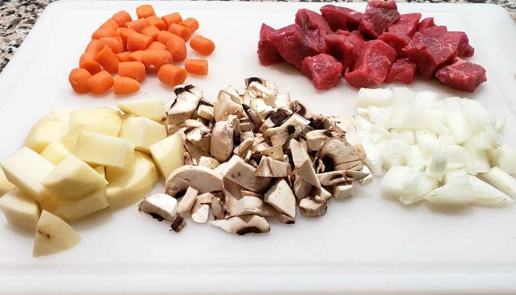 zanahorias picadas, estofado de carne, papas, champiñones y cebollas en una tabla para cortar