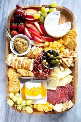 Charcuterie board with meats, sliced cheese, dips, crackers and fruit, served on a wood board.