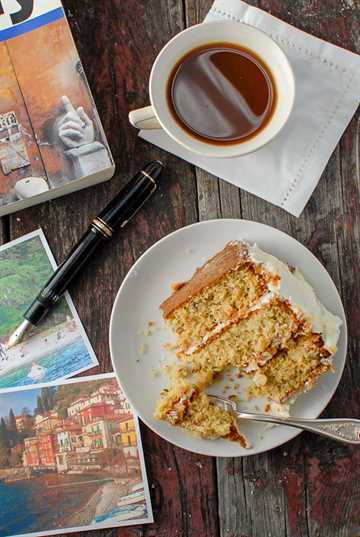 Rebanada parcial de pastel de crema italiana con una taza de café y un libro de viajes.