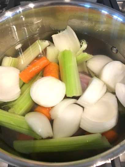 Cuello de pavo y menudillos con zanahorias, cebollas y apio en agua en una olla.
