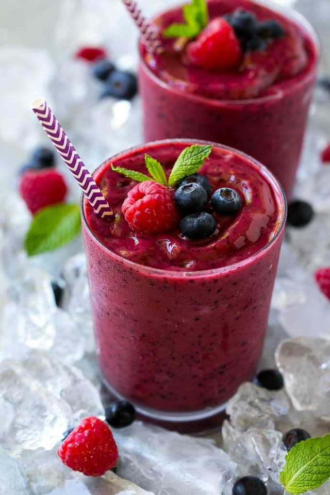 A glass of frozen fruit smoothie in crushed ice, garnished with berries and mint.