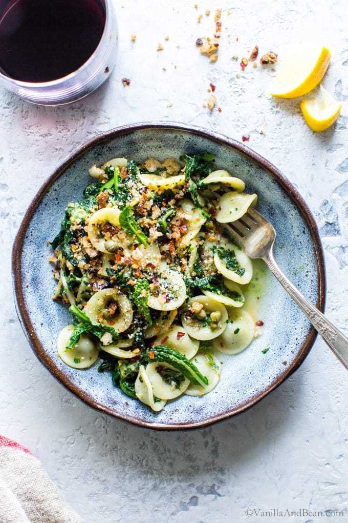 Orecchiette with Garlicky Kale and Breadcrumbs in a bowl with a fork and wine on the side.