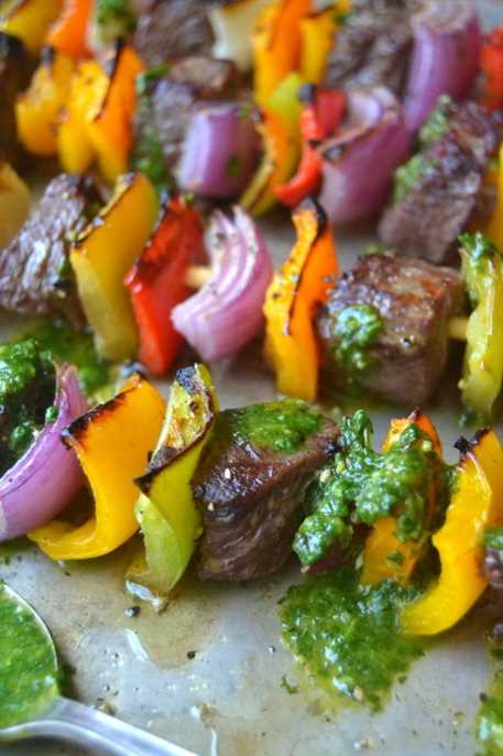 Steak fajita skewers lined up on a baking sheet drizzled with cilantro pesto