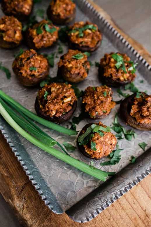 stuffed mushrooms sprinkled with cilantro on a silver tray with scallions on the side
