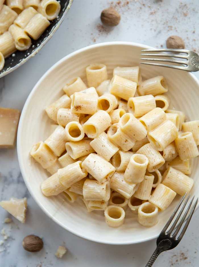 overhead shot of pasta in white bowl with parmesan and whole nutmegs garnished around