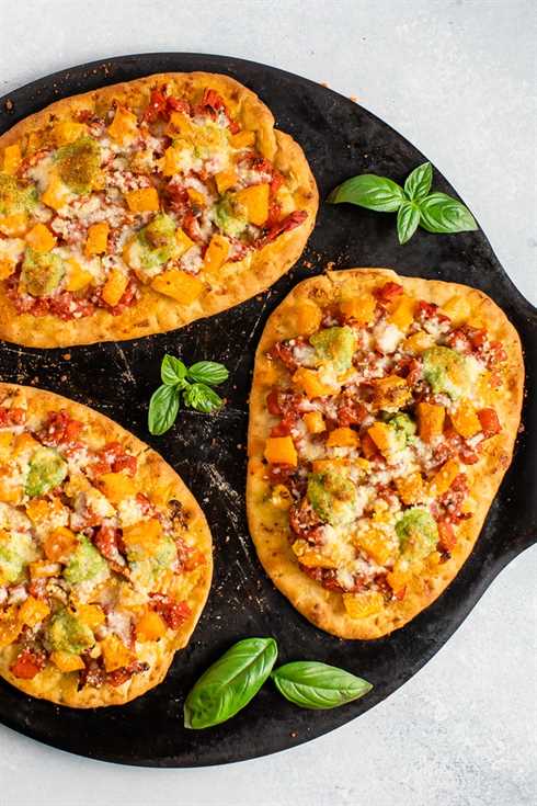 Three naan pizzas with butternut squash and pesto on a round baking stone.