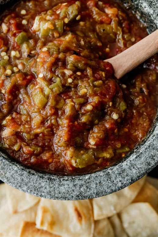 close up shot of homemade salsa with canned tomatoes and green chiles in a stoneware bowl molcajete with a wooden spoon