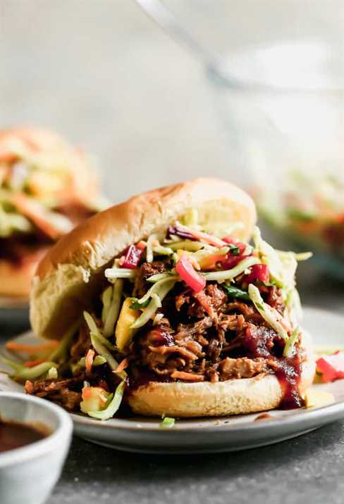 A BBQ pulled pork sandwich with slaw, in a bun, served on a plate.