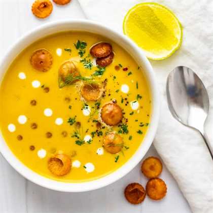 Curried pumpkin soup in a bowl with croutons and a lime wedge.