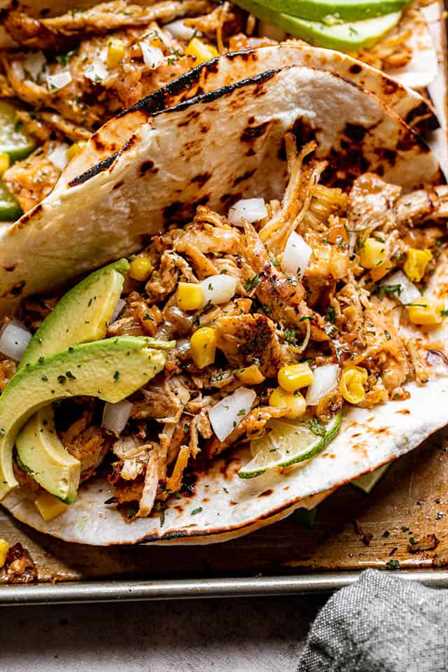 close up shot of a taco filled with chicken carnitas, avocado slices, corn, and onions