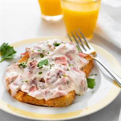 A serving of creamed chipped beef on toast with a fork and orange juice.