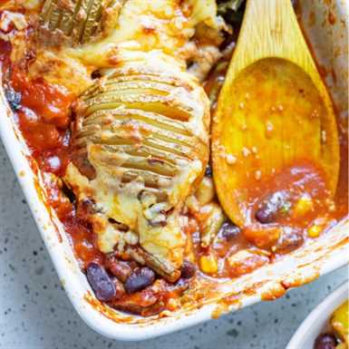 Wooden spoon in a white casserole dish serving up chili and hasselback potatoes with cheese