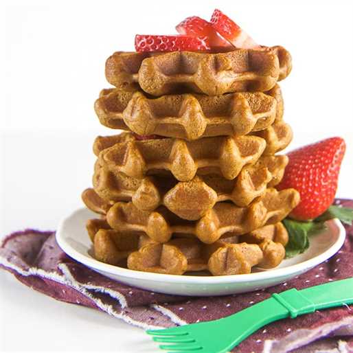 A stack of healthy gingerbread waffles on a white plate with fresh strawberries.
