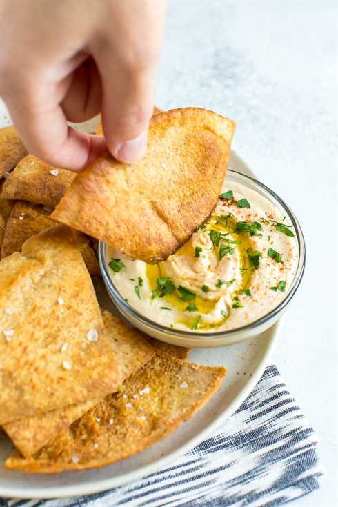 Hand dipping a pita chip into a bowl of hummus.