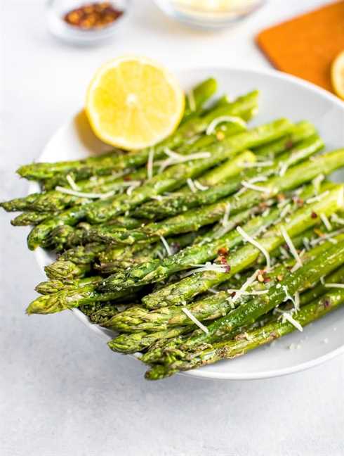 Roasted asparagus in a bowl, topped with parmesan, red pepper flakes, and fresh lemon.