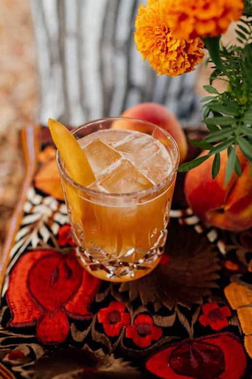 bourbon peach old fashioned with a peach garnish in a crystal glass on a red and orange tablescape with marigolds