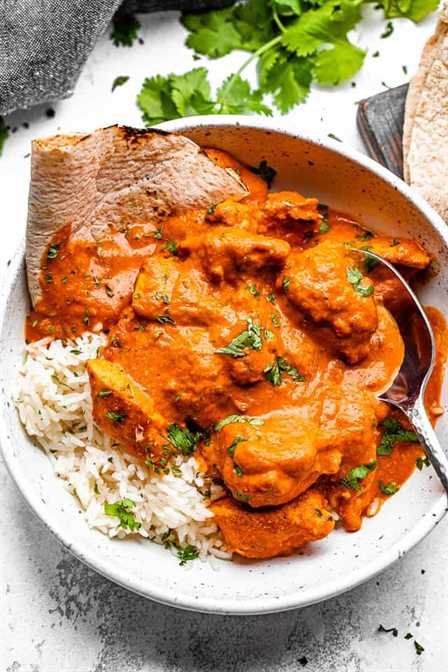 Chicken tikka masala in a bowl with rice and naan and a metal spoon
