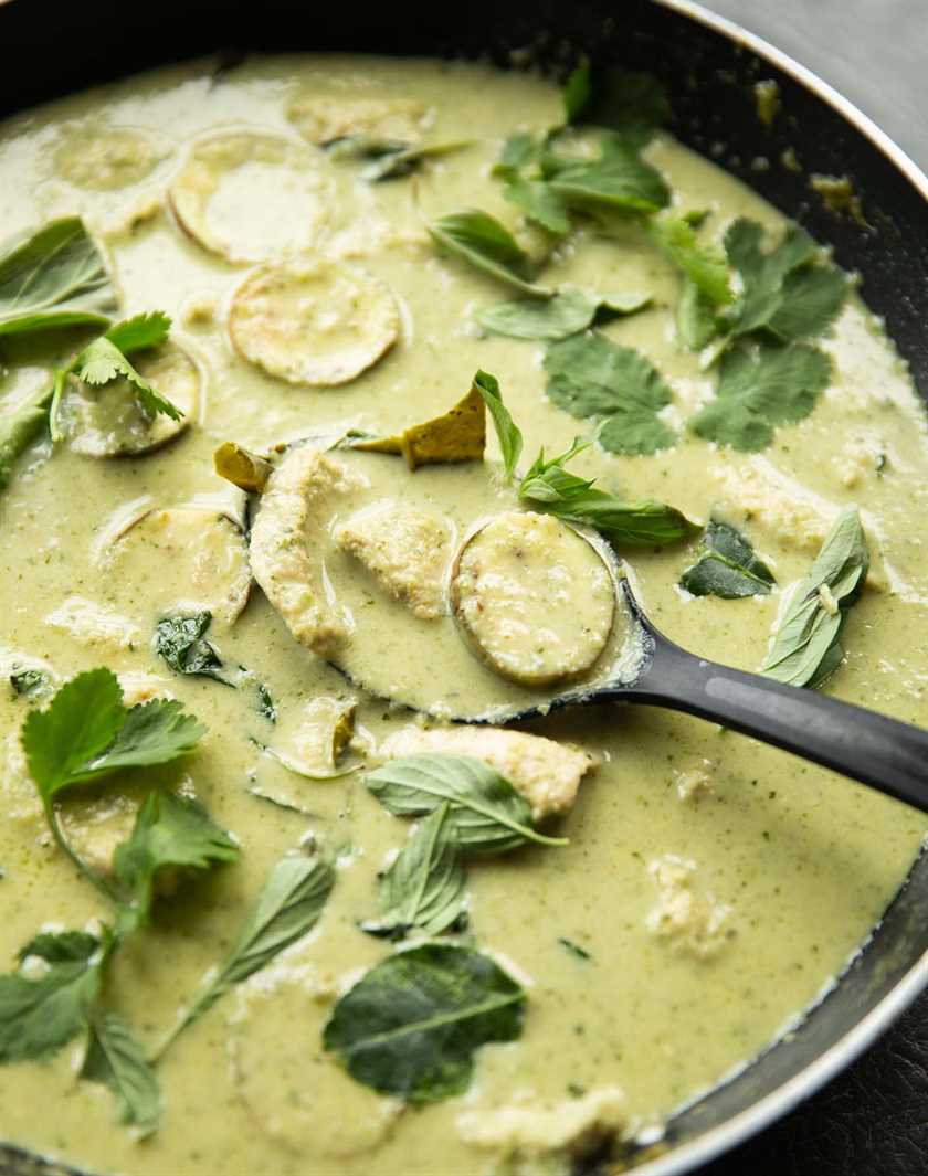 black serving spoon digging in to large pan of green curry