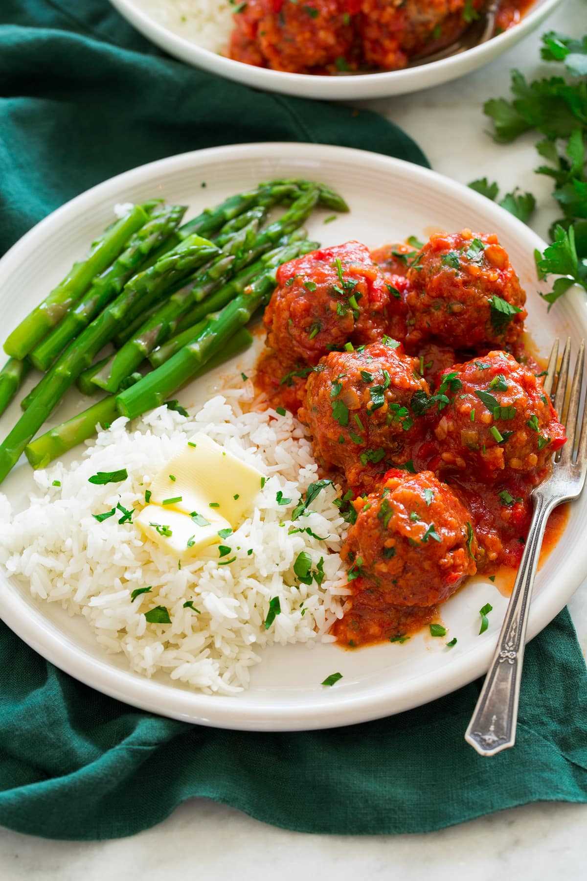 Porcupine Meatballs shown on a large white plate with sides of rice and butter and steamed asparagus.