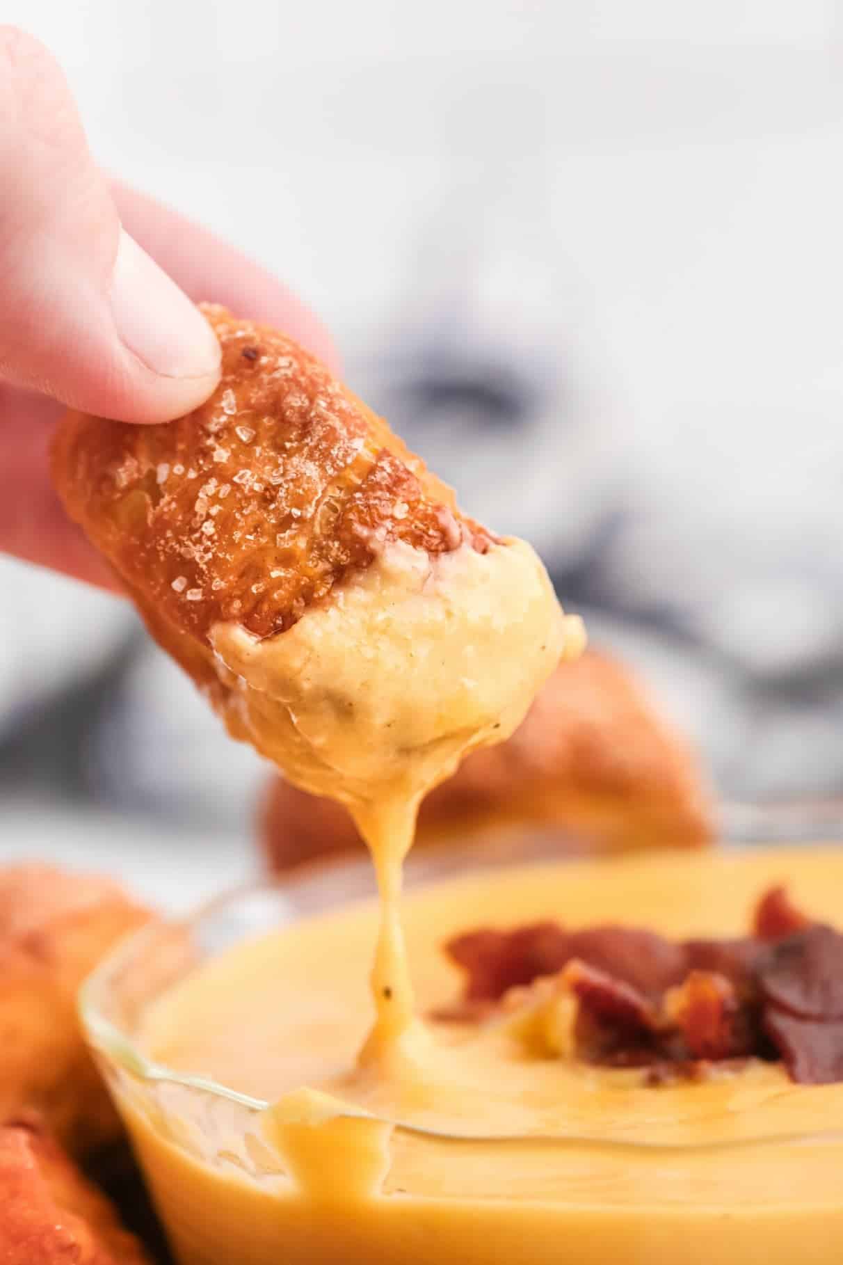 A pretzel bite being dipped in beer cheese sauce.