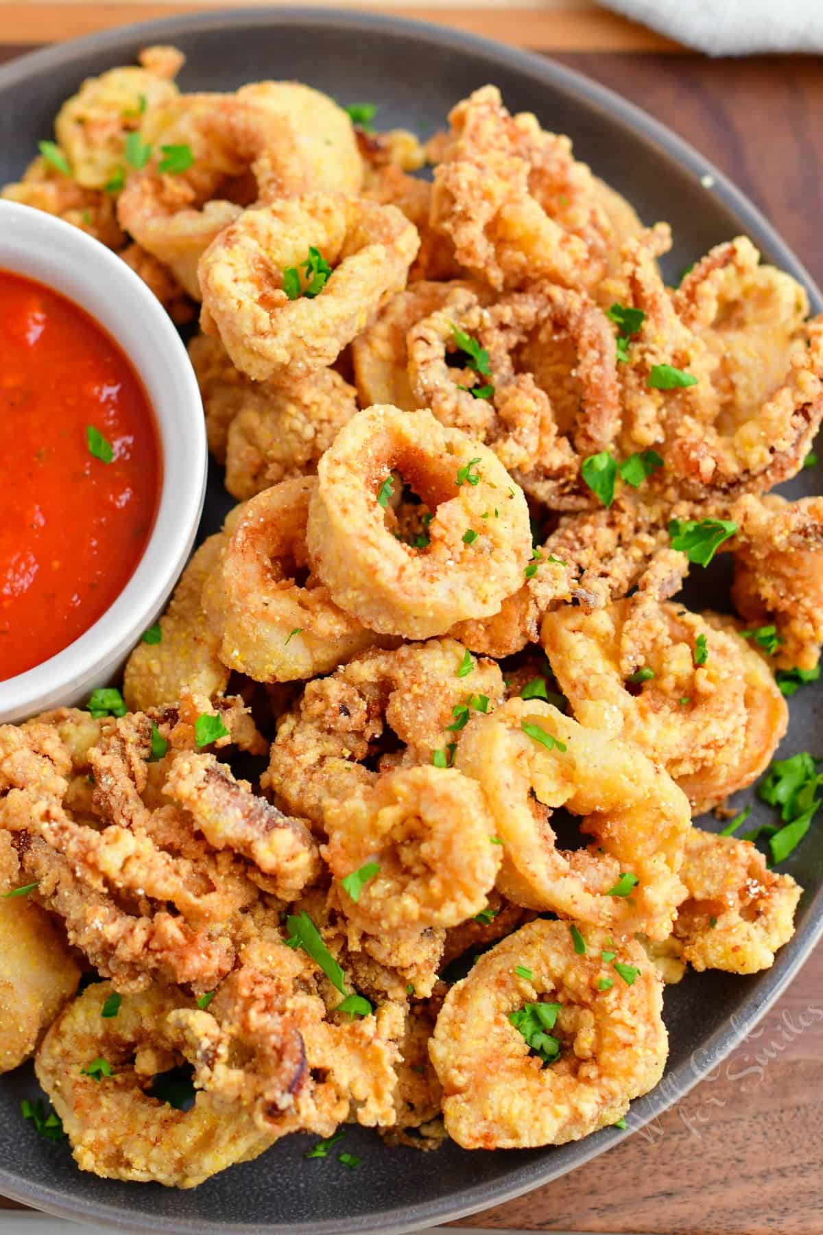 Calamari is plated with a small bowl of red dipping sauce.