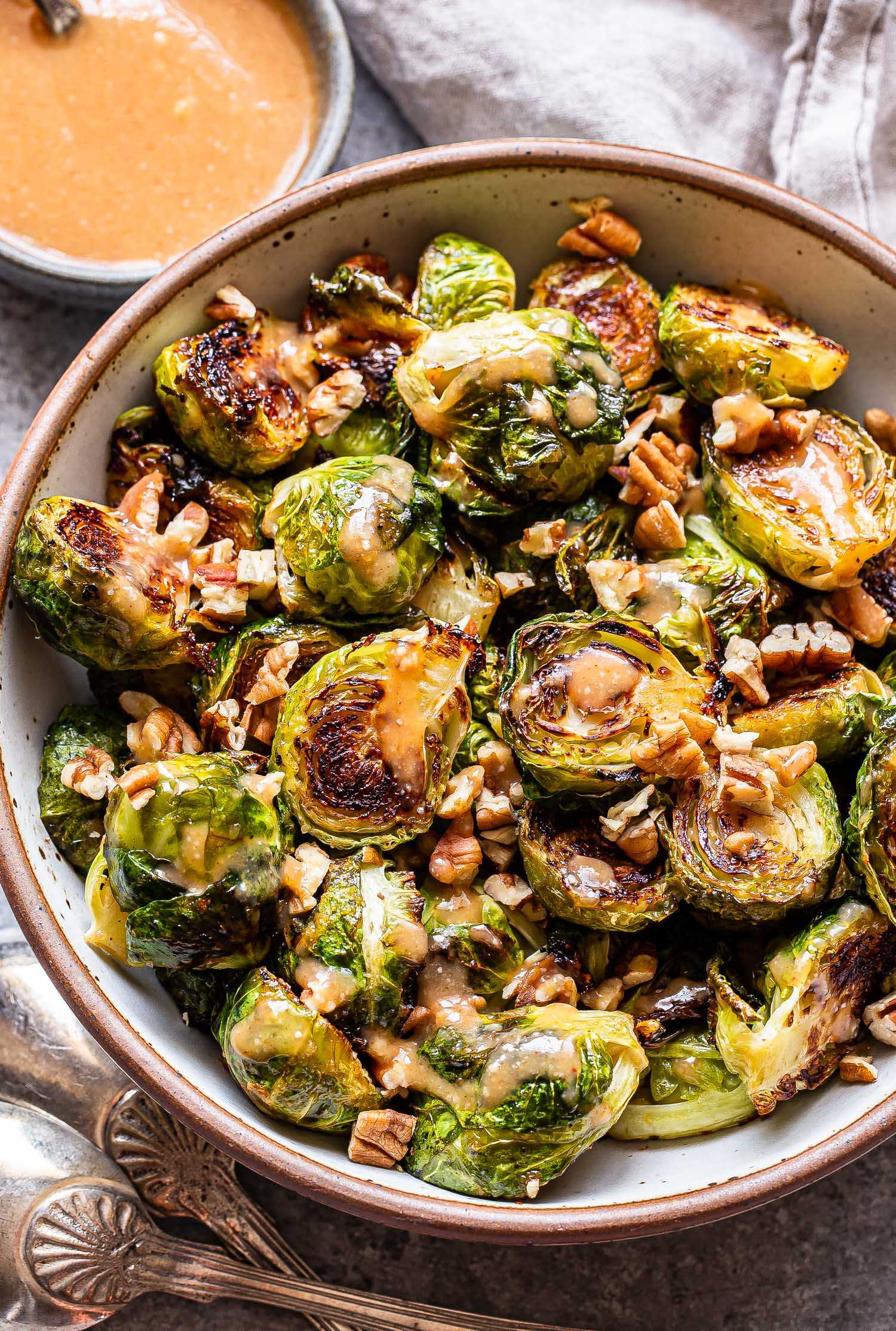 Miso roasted brussels sprouts in a white bowl with a small bowl of dressing behind them.