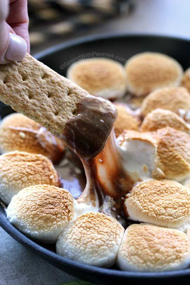 taking a serving of Hot Smores Dip from the skillet on a graham cracker