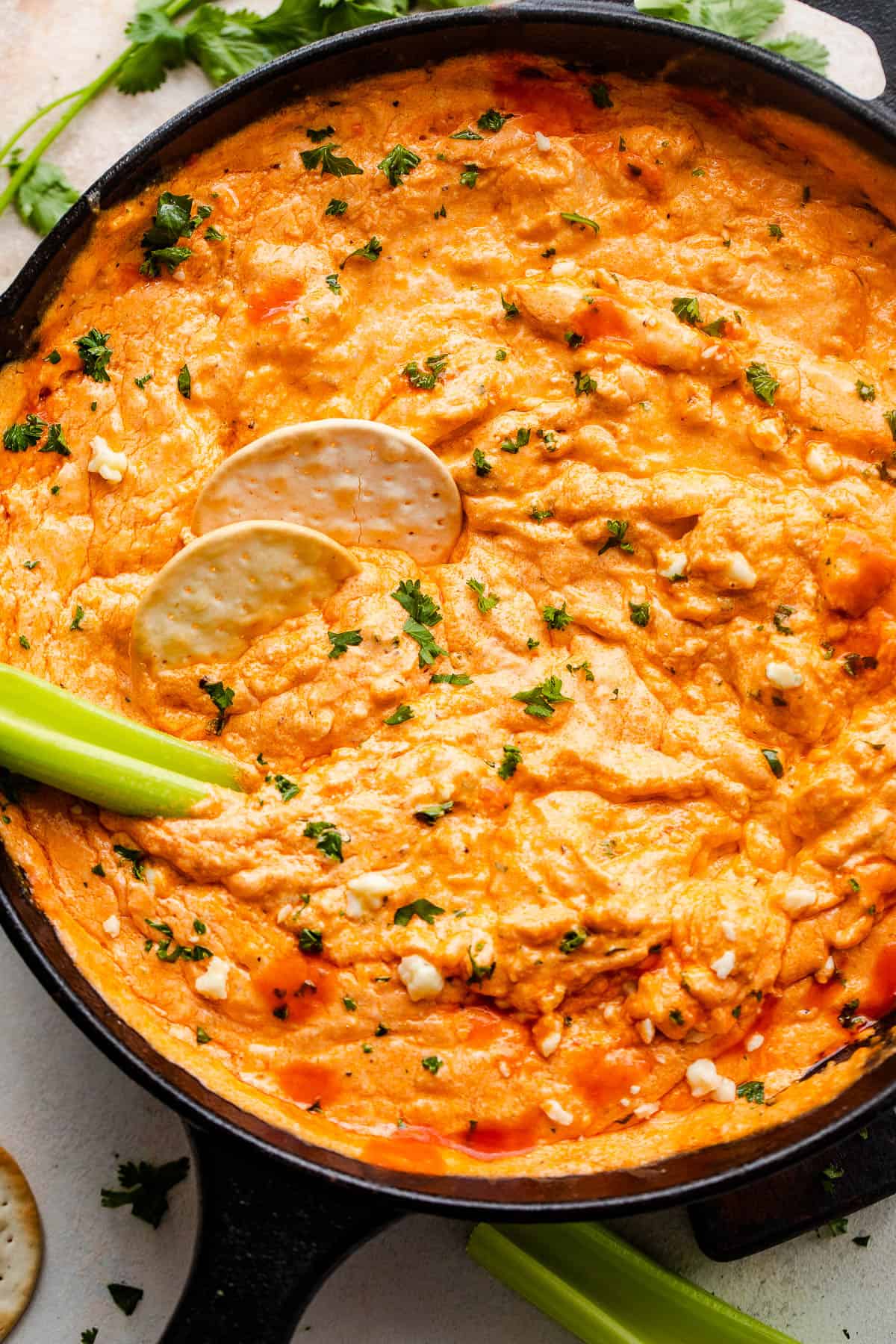 overhead shot of buffalo chicken dip in a cast iron skillet with two crackers and celery sticks in the dip