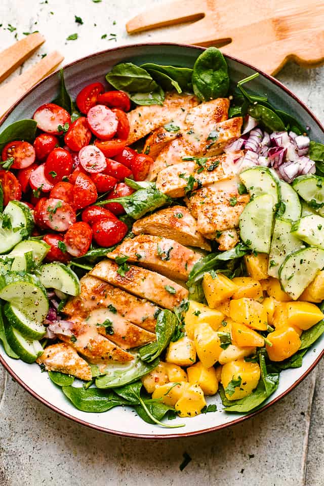sliced chicken breasts, chopped mangoes, sliced cucumbers, and halved cherry tomatoes set over a bed of lettuce