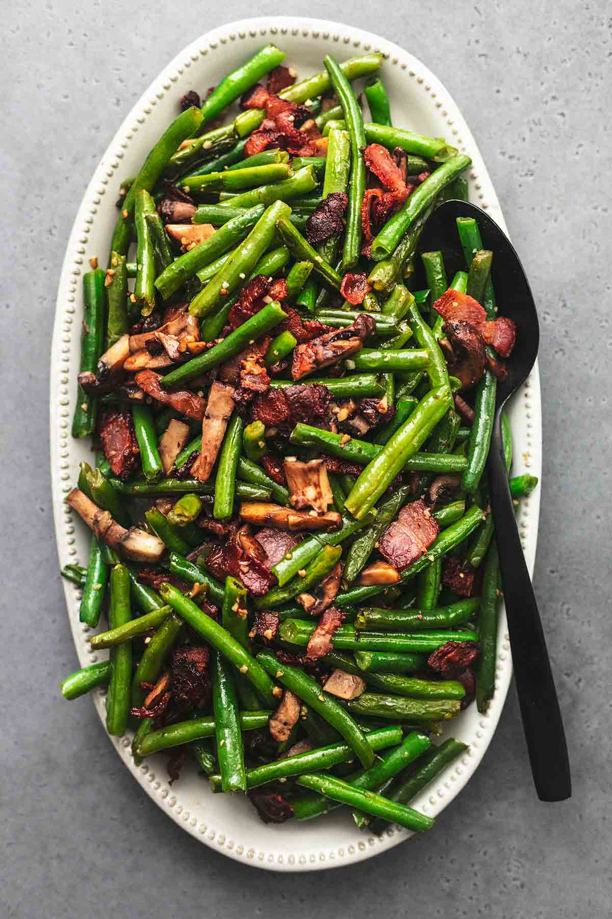 top view of green beans with mushrooms and bacon with a serving spoon on a platter.