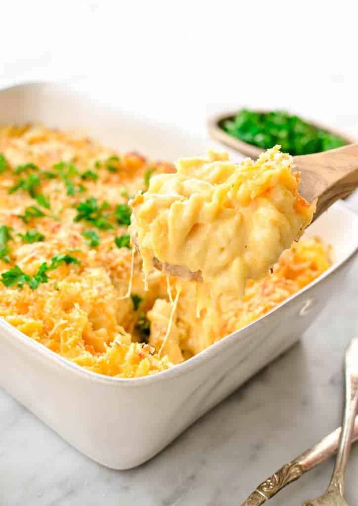 Baking dish with greek yogurt mac and cheese with a scoop being taken out with a wooden spoon