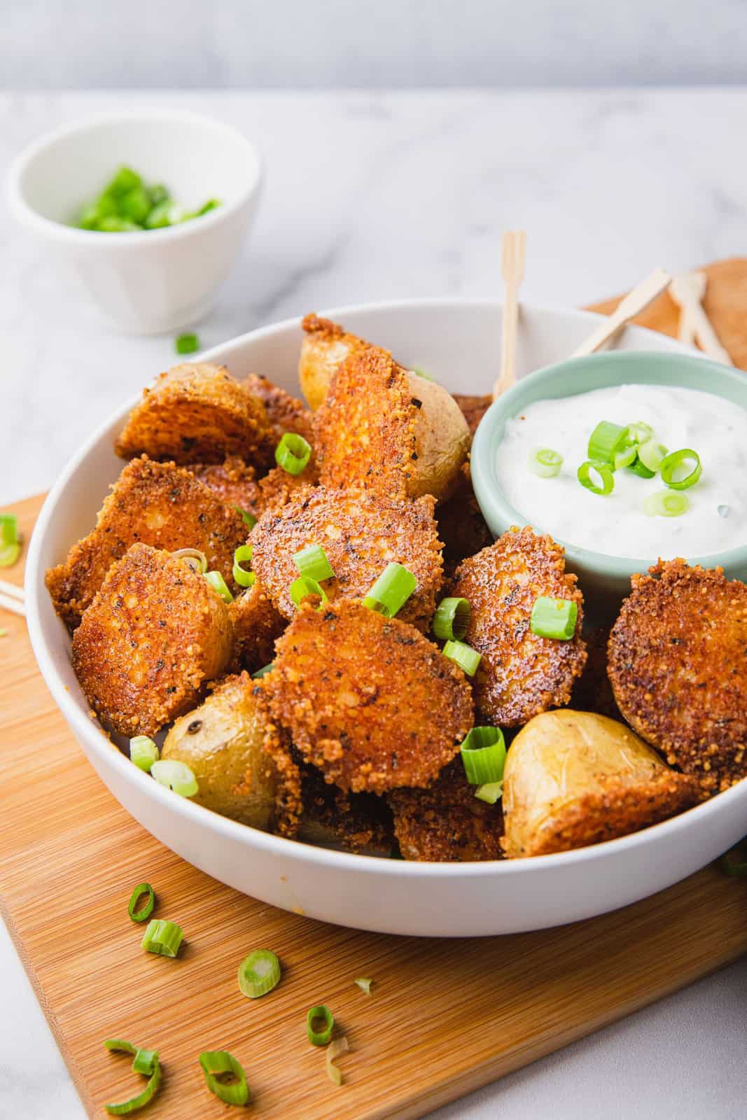 White bowl with Crispy Parmesan Potatoes with dipping sauce and green onions