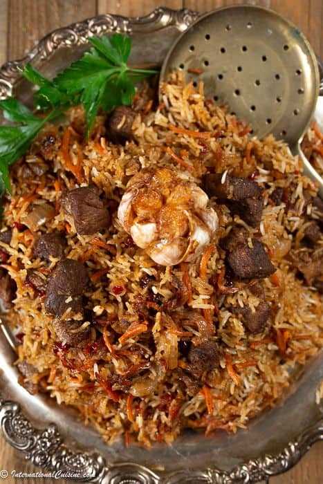 a platter full of Uzbek plov with lamb pieces, carrots, a whole roasted garlic and of course seasoned rice.