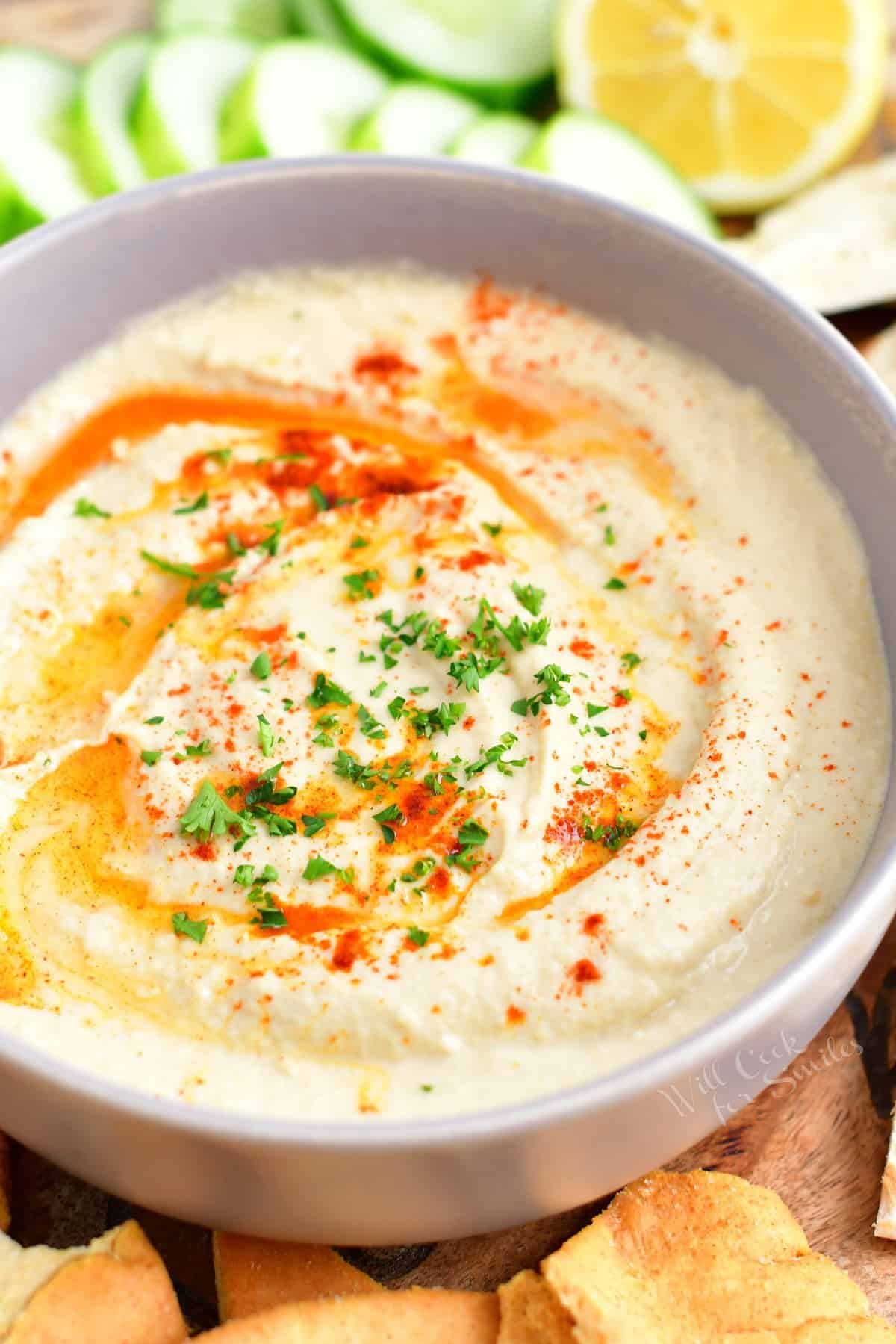 A white bowl filled with hummus is ready to be eaten.