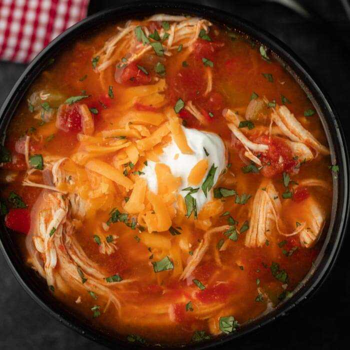 Close up of a black bowl of chicken fajita soup topped with sour cream and shredded cheddar cheese
