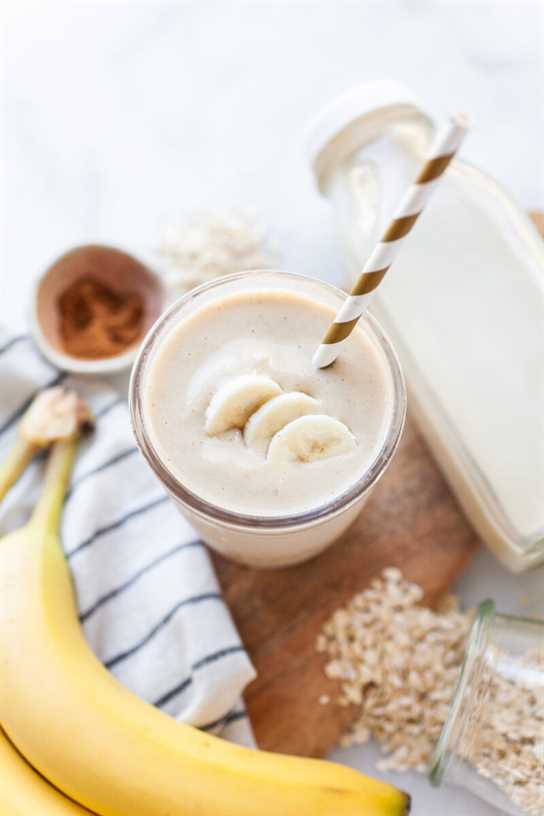 image of an oat milk smoothie topped with banana slices on a board with bananas and oat milk beside it