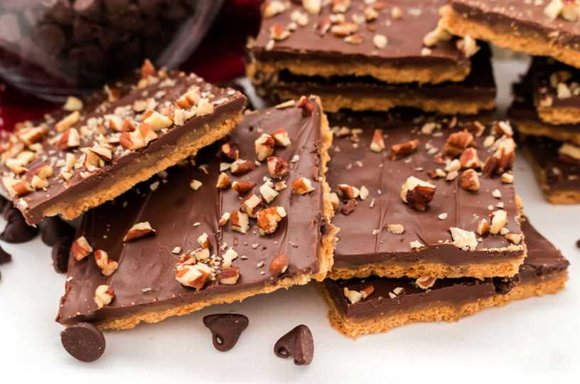Closeup on a stack of Graham Cracker Toffee pieces arranged on a white surface surrounded by chocolate chips.