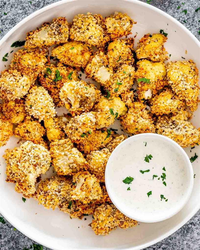 baked breaded cauliflower in a white bowl with ranch dressing.