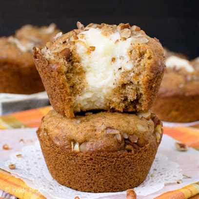 Two carrot cheesecake muffins stacked on top of each other with a bite out of the top one showing the creamy filling