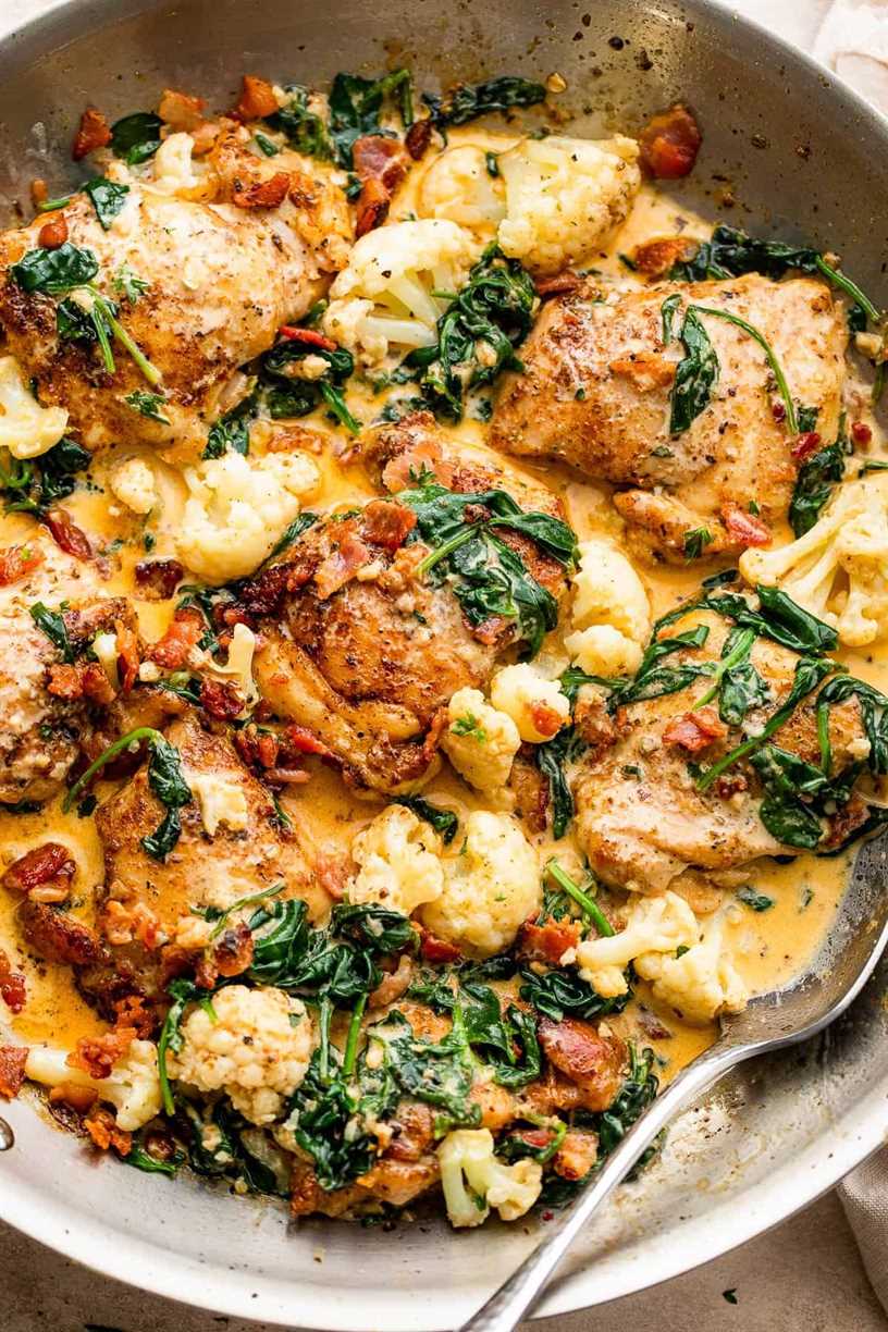 close up shot of cooked boneless chicken thighs topped with baby spinach, cream sauce, cauliflower, and bacon