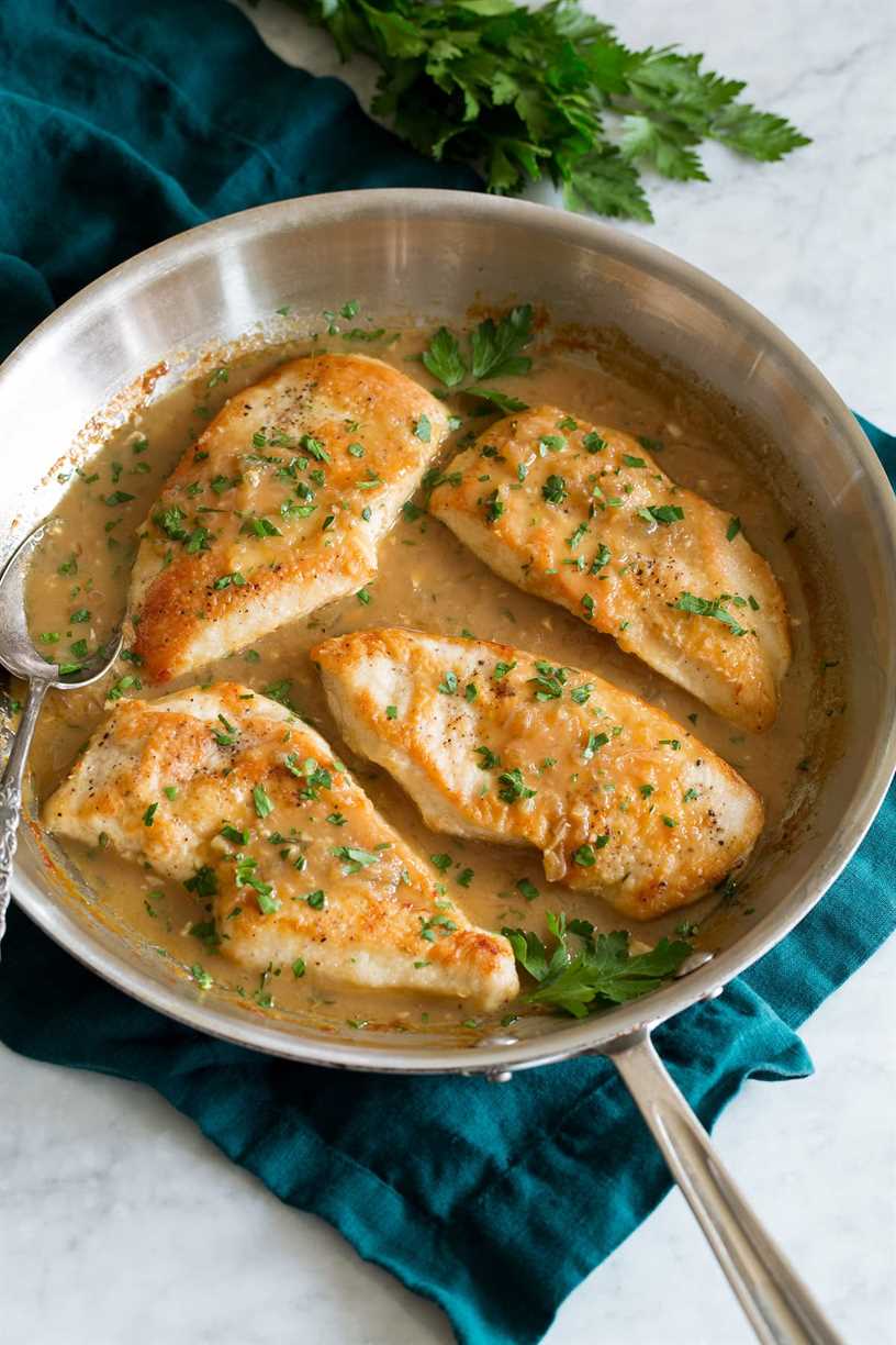 Chicken breasts in white wine and onion sauce in a skillet.