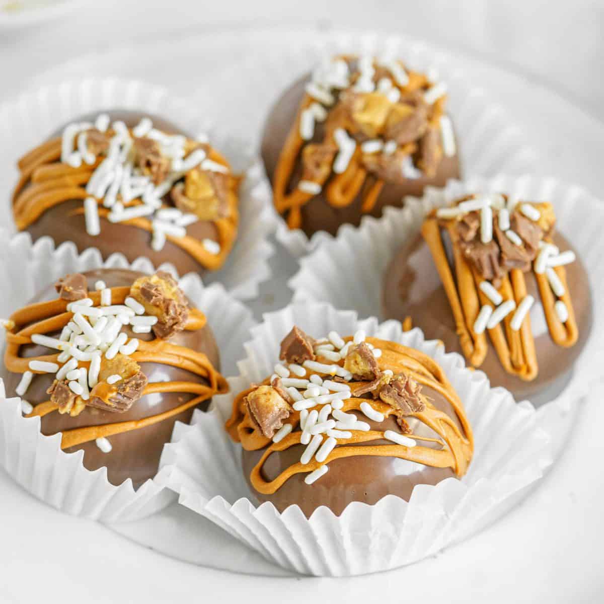 Square image of Chocolate Peanut Butter Hot Cocoa Bombs in paper liners on white plate.
