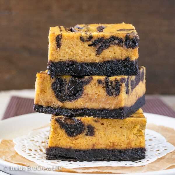 Three pumpkin cheesecake brownies stacked on top of each other.