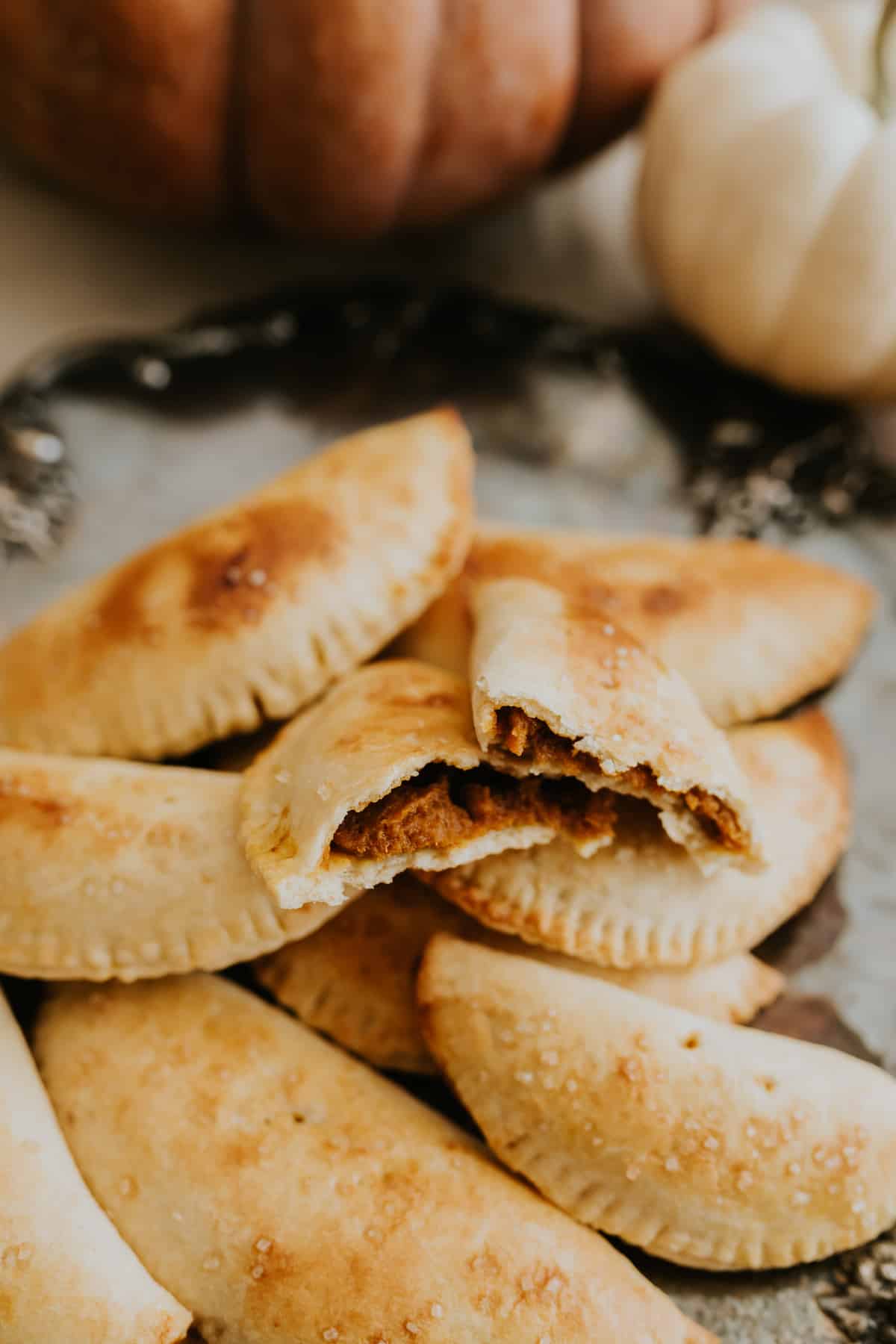 Pumpkin empanadas on a vintage metal plate with pumpkins in the background